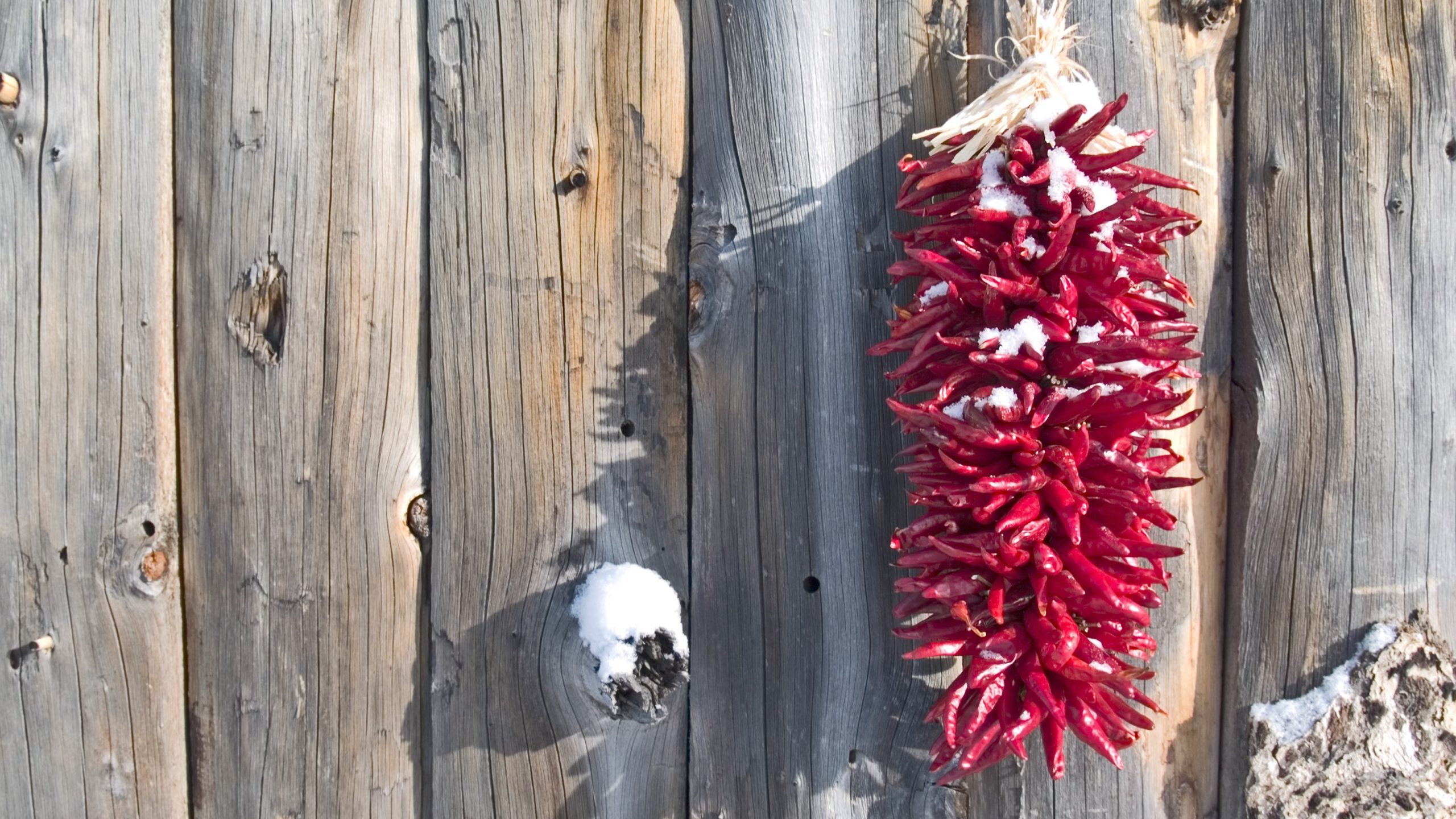 iStock-93356032_edited Light round wood vertical latillas with red ristra hanging on the right all dusted in snow.