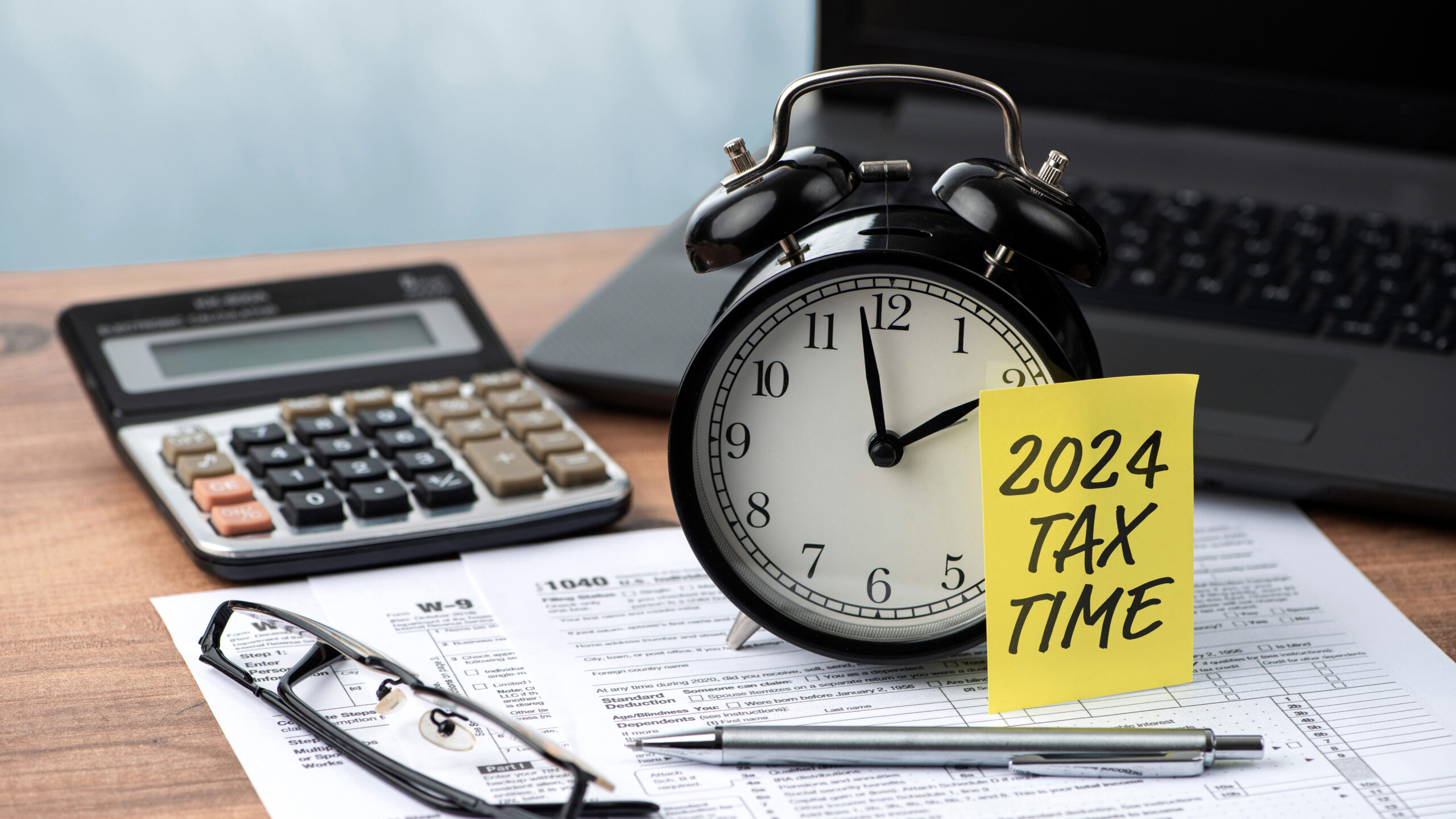 iStock-1813544838_w wood des with tax forms, glasses, calculator, and post it for 2024 saying Tax Time