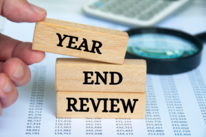 Wood blocks with words, Year, End, Review on top of papers with columns of numbers and magnifying glass in background